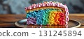 Colorful rainbow cake slice with vibrant layers on a wooden plate surrounded by sprinkles 131245894