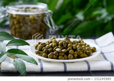 pickled caper buds in a plate on a black marble background, selective focus. Canned capers. 131245995
