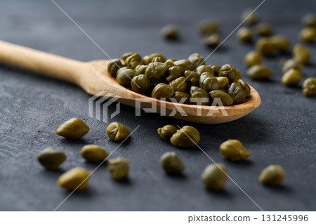 Marinated capers in a wooden spoon on a black marble background,  selective focus. 131245996