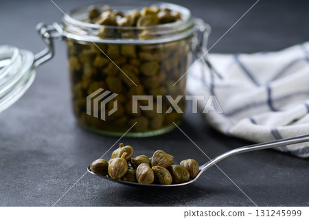 open jar of marinated capers on a black marble background, selective focus. open jar of marinated capers on a black marble background, selective focus. 131245999