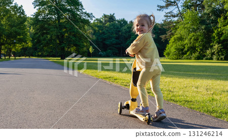 Scooter child. Girl riding scooter toddler. Yellow outdoor activity park road. 131246214
