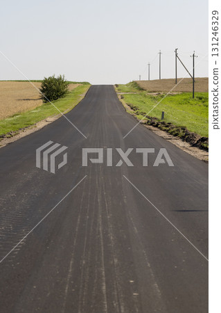 black new asphalt on the highway against the background of the blue sky, a newly built asphalt highway made of bitumen with crushed stone and sand in the countryside 131246329