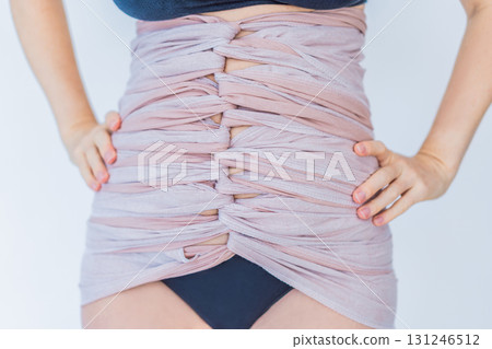 Postpartum woman wraps her belly using Bengkung, a traditional Malaysian belly binding method. Concept of postpartum recovery, cultural practice, and natural healing support 131246512