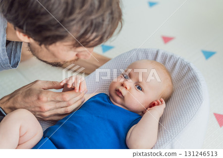 Loving father interacts with his 3-month-old baby lying in a cozy baby nest at home. Tender bonding moment, fatherhood, and early connection in a peaceful family setting Loving father interacts with his 3-month-old baby lying in a cozy baby nest at home. Tender bonding moment, fatherhood, and early connection in a peaceful family setting 131246513
