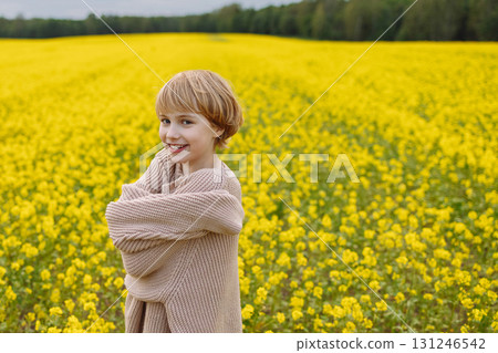 Smiling girl in oversized beige sweater hugging herself in yellow flower field 131246542