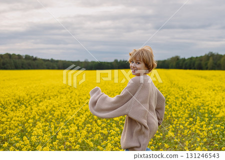 Smiling girl in beige sweater running in yellow flower field looking at camera Smiling girl in beige sweater running in yellow flower field looking at camera 131246543
