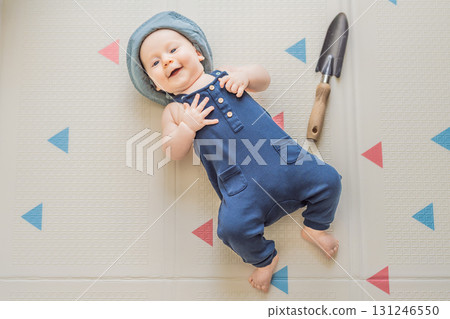 Adorable baby dressed as a little gardener with a small garden shovel nearby. Concept of gardening, nature connection, and playful early childhood imagination Adorable baby dressed as a little gardener with a small garden shovel nearby. Concept of gardening, nature connection, and playful early childhood imagination 131246550