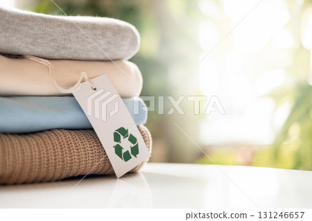 Stack of folded sustainable clothes with recycling tag on white table, eco-friendly concept 131246657
