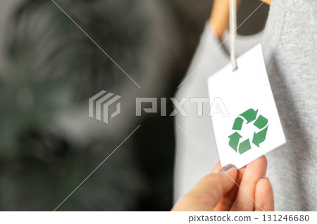Hand holding eco-friendly tag with recycle symbol on gray sustainable clothing in soft focus 131246680