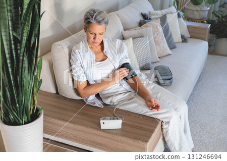 Senior woman checks blood pressure at home with digital monitor, daily health care routine Senior woman checks blood pressure at home with digital monitor, daily health care routine 131246694