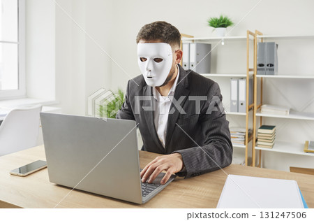 Anonymous man in face mask uses laptop computer for online business or internet scam 131247506