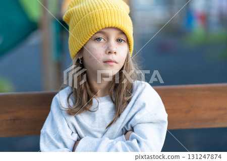 Serious girl in cap sitting arms crossed on bench Serious girl in cap sitting arms crossed on bench 131247874