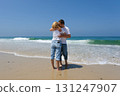 Couple embracing near the edge of the sea with waves touching their feet on a bright sunny beach. 131247907