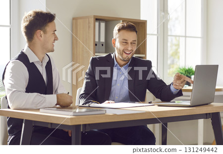 Two smiling business men working in office sitting with laptop computer. Two smiling business men working in office sitting with laptop computer. 131249442
