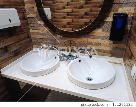 modern bathroom interior with two sinks, a faucet and a round mirror modern bathroom interior with two sinks, a faucet and a round mirror 131251122