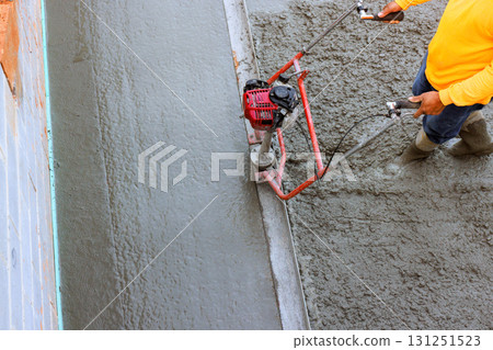 Construction worker operates concrete finishing machine on smooth surface during leveling concrete Construction worker operates concrete finishing machine on smooth surface during leveling concrete 131251523