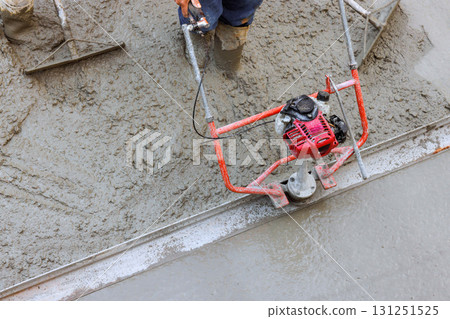 Worker uses troweling machine to finish leveling concrete on construction site under works day Worker uses troweling machine to finish leveling concrete on construction site under works day 131251525