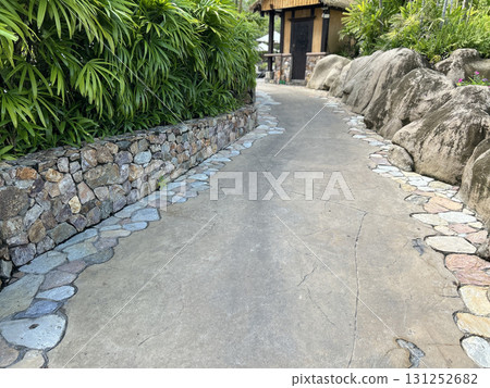 Stone lined garden pathway with lush foliage and rocks 131252682