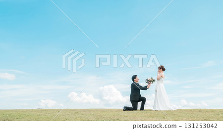 A groom kneeling and handing over a bouquet to a bride in a dress (wedding, wedding ceremony, bridal, photo wedding) 131253042