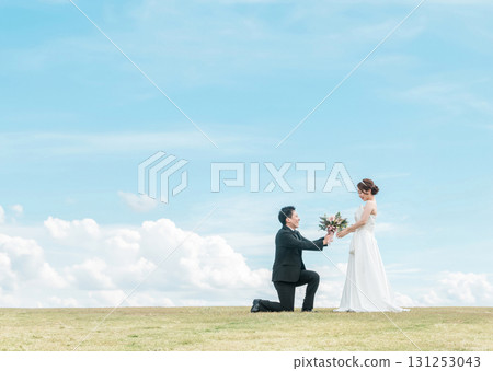A groom kneeling and handing over a bouquet to a bride in a dress (wedding, wedding ceremony, bridal, photo wedding) 131253043