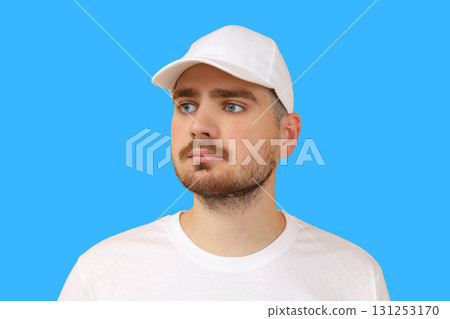 Young man poses in white cap and t-shirt against blue backdrop Young man poses in white cap and t-shirt against blue backdrop 131253170