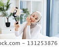 Young adult Muslim woman with hijab applying facial cream while using smartphone for vlogging. Captures concept of modern self-care and engagement through social media. 131253876