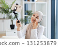 Young Muslim woman in her 20s recording skincare video applying facial cream indoor setting. Promotes self-care, beauty, and digital content creation. 131253879