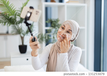 Young Muslim woman in her 20s recording skincare video applying facial cream indoor setting. Promotes self-care, beauty, and digital content creation. Young Muslim woman in her 20s recording skincare video applying facial cream indoor setting. Promotes self-care, beauty, and digital content creation. 131253879