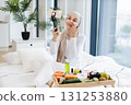 Young Muslim woman in hijab recording video about skincare using natural products in comfortable home environment filled with natural light and decor. Promotes healthy skincare routines and home 131253880