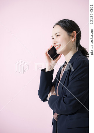 一位身穿西裝的年輕女商人在粉紅色背景下打電話的側面照 131254591