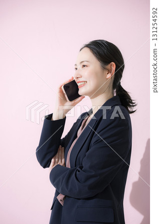 Profile of a young business woman in a suit making a phone call on a pink background Profile of a young business woman in a suit making a phone call on a pink background 131254592