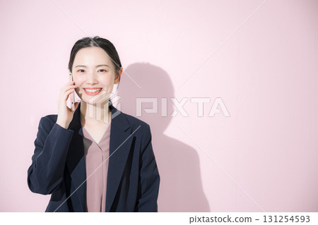 Front view of a young business woman in a suit making a phone call on a pink background 131254593