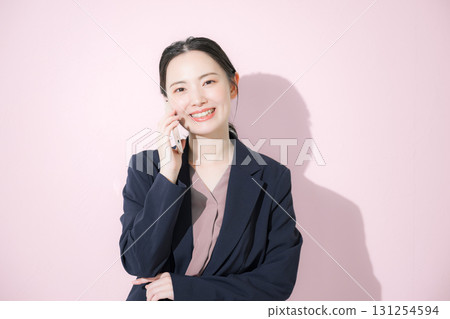 Front view of a young business woman in a suit making a phone call on a pink background Front view of a young business woman in a suit making a phone call on a pink background 131254594