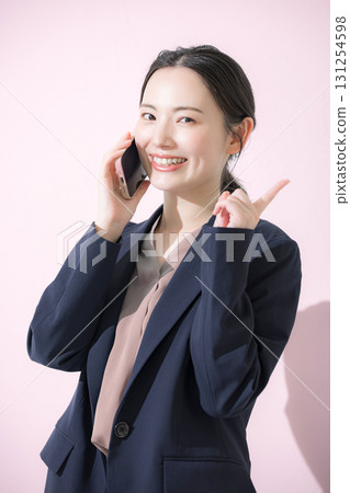 一位身穿西裝的年輕女子在粉紅色背景下打電話、指著某樣東西並推薦它的正面肖像 131254598
