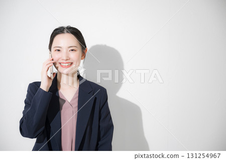 Front view of a young woman in a suit making a phone call 131254967