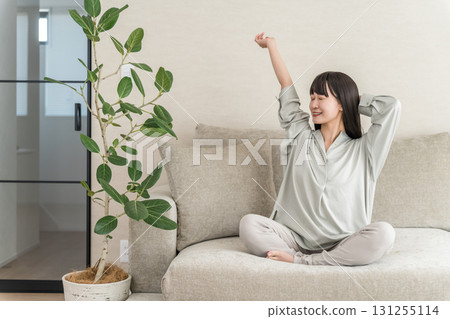 年輕的亞洲女性在家裡的沙發上放鬆和提神（早上的例行公事） 131255114
