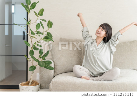 年輕的亞洲女性在家裡的沙發上放鬆和提神（早上的例行公事） 131255115