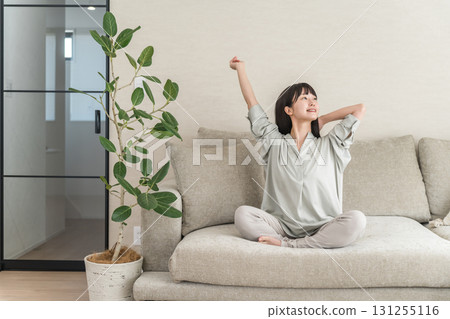 年輕的亞洲女性在家裡的沙發上放鬆和提神（早上的例行公事） 131255116