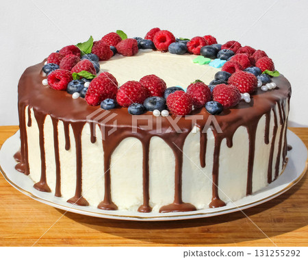 Cake in chocolate, decorated with blueberries, raspberries and green leaves on a white background. Picture for a menu or a confectionery catalog. Cake in chocolate, decorated with blueberries, raspberries and green leaves on a white background. Picture for a menu or a confectionery catalog. 131255292