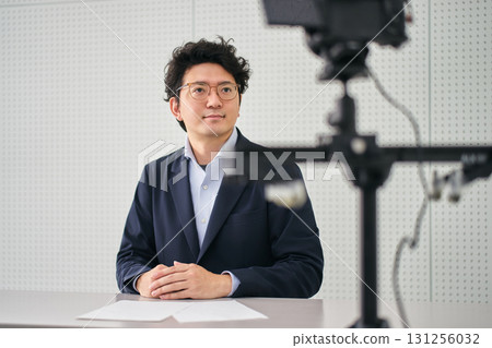 A male newscaster reading a script in front of a camera in a broadcasting studio 131256032
