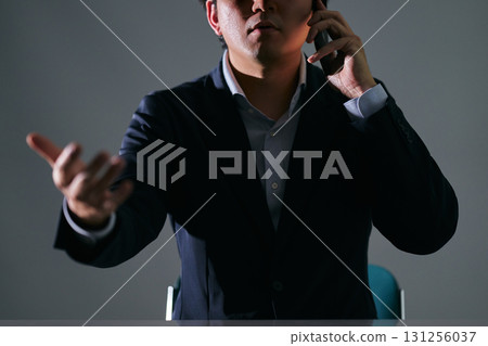 一位憤怒的、不道德的商人穿著西裝，在黑暗的房間裡用智慧型手機與對方爭吵 131256037