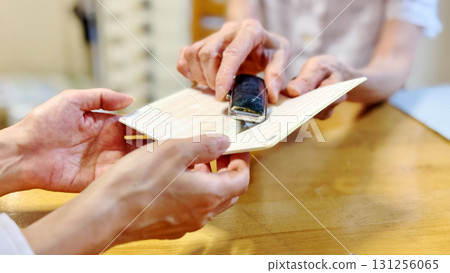 Elderly woman handing an open bankbook and seal case to another woman_wide Elderly woman handing an open bankbook and seal case to another woman_wide 131256065