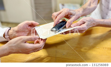 Elderly woman handing over bankbook and seal case to another woman_wide Elderly woman handing over bankbook and seal case to another woman_wide 131256069