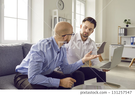 Two young business men working in office on a laptop, talking and having discussion. 131257547