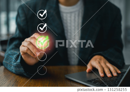 A business professional uses a digital checklist for assessment, highlighting a green check mark on a transparent screen interface. A business professional uses a digital checklist for assessment, highlighting a green check mark on a transparent screen interface. 131258255