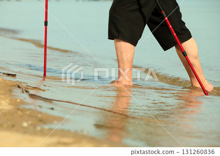 barefoot senior nordic walking on a beach. 131260836
