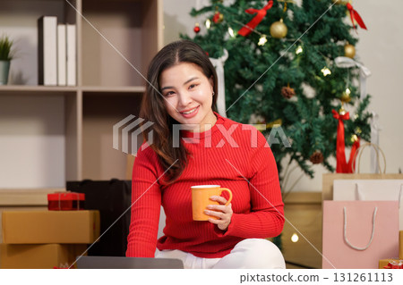 Christmas cheer. Woman enjoying hot drink while working on laptop at home. 131261113