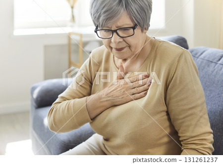 Senior woman sitting alone on sofa in the living room at home suffering from heart attack. 131261237