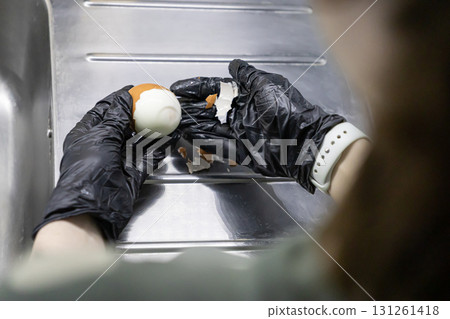 Person wearing black protective gloves carefully peeling a hard-boiled egg over a clean stainless steel sink, emphasizing food hygiene, safety, and cooking 131261418
