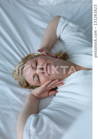 woman applying sheet mask at home in front of double sided mirror.beautiful girl in white robe sitting with coffee or tea cup in hand. relax and wellbeing moment. lot of cosmetic in front of female. 131261623